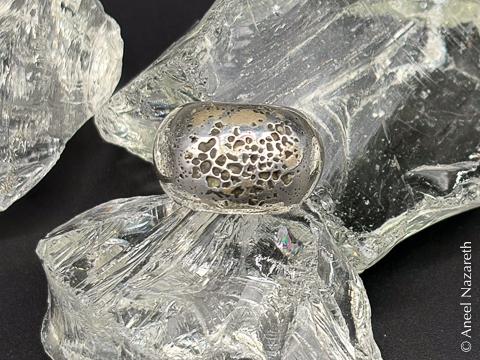 The ring is photographed among some pieces of glass. It has many deep pits in it, looking almost like lunar craters